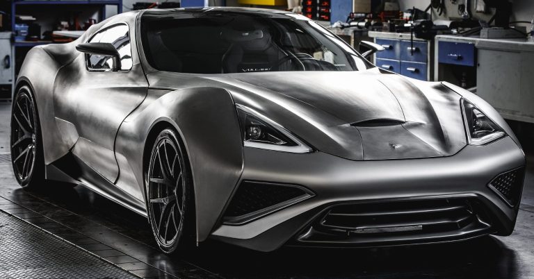Sleek grey sports car with an aerodynamic design in a workshop setting.