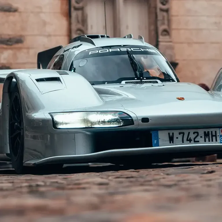 Silver Porsche 963 RSP with aerodynamic design parked on cobblestone street.